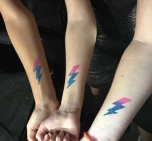 Four mitzvah attendees displaying their arms with matching lightning bolt tattoos of a custom bat or bar mitzvah logo