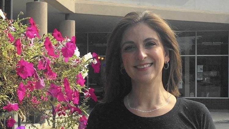 A woman smiling outdoors next to vibrant pink flowers.