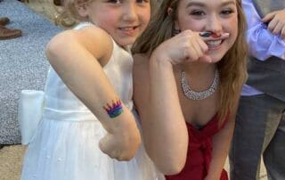 A bridesmaid and a flower girl showing off a temporary tattoo at an outdoor wedding reception