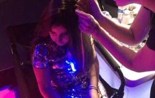 A stylist is applying makeup to a seated girl. Hair adornments make wonderful bat mitzvah activities.